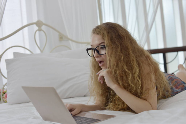 European woman lying in bed and using laptop - Фото, изображение