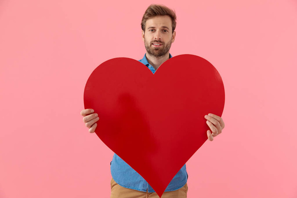 happy casual guy smiling and holding big red heart - Foto, Bild