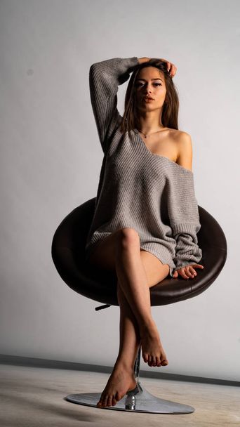 beautiful sexy girl, posing a short gray dress, a white background chair - Photo, image