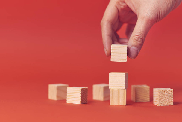 Hand arranging wood cube stacking. Business concept growth success process on red background, copy space. - Foto, Imagen