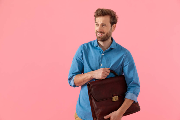 デニムシャツのハッピーカジュアルな男が笑顔でスーツケースを持ち - 写真・画像
