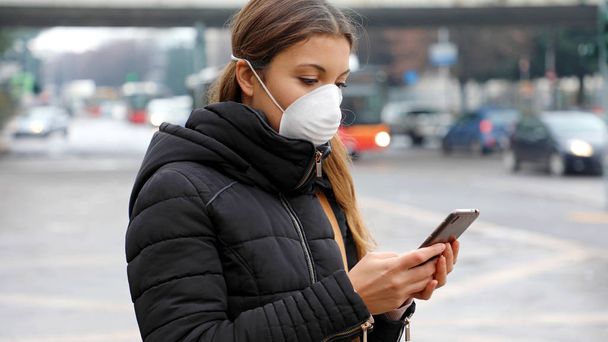 COVID-19 Pandemic Coronavirus Young Woman Using Smart Phone in City Street Wears Face Mask через Ковід-19, забруднення повітря, партикулати, грип Virus або інфлюенцу - Фото, зображення
