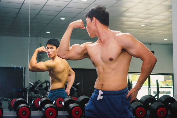 Asian young man flexing his muscles in front of a glass in the g - Foto, Imagem