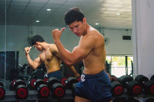 Asian young man flexing his muscles in front of a glass in the g - Foto, Imagen