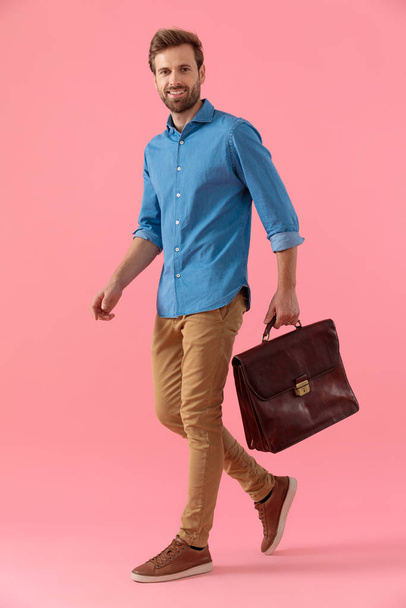 happy casual guy in denim shirt holding suitcase and smiling - Foto, imagen