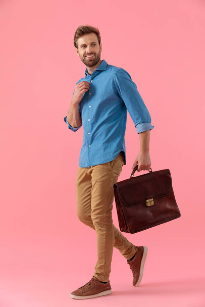 happy casual man holding suitcase and fixing shirt - Photo, image