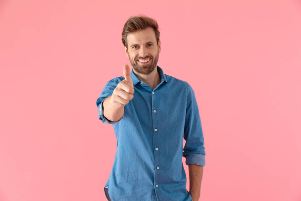 casual young man smiling and making thumbs up sign - Fotoğraf, Görsel