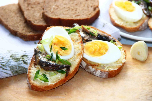 Přípitek. Sendviče na žitném chlebu s vejcem a šproty na dřevěné desce - Fotografie, Obrázek