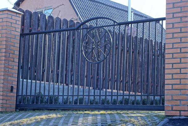 puerta de hierro negro de varillas de hierro forjado con un patrón y parte de una cerca de ladrillos marrones en la calle
 - Foto, imagen