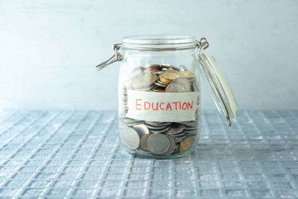 Монеты в стеклянной банке с этикеткой образования, финансовая концепция. - Фото, изображение