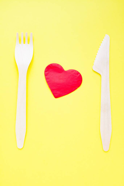 Bamboo biodegradable fork and knife made of natural eco recycle reusable material and paper heart on yellow. - Valokuva, kuva