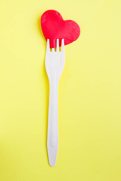 Bamboo biodegradable fork made of natural eco recycle reusable material and paper heart on yellow background. Healthy food for heart or eco love - Zdjęcie, obraz