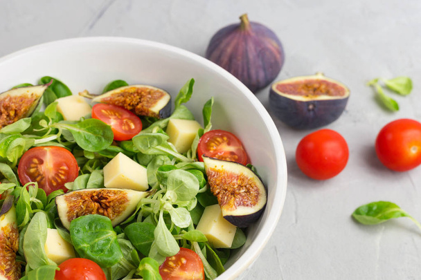Fresh salad with figs, green leaves, cherry tomatoes and cheese on gray background. Free space for text. Top view. Abstract food background with big plate - Photo, Image