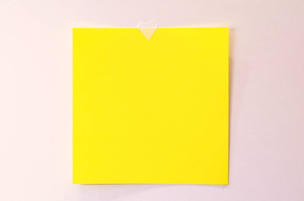 Bright yellow paper sheet sticked with a heart to a white wall. Copy space for text - Fotografie, Obrázek