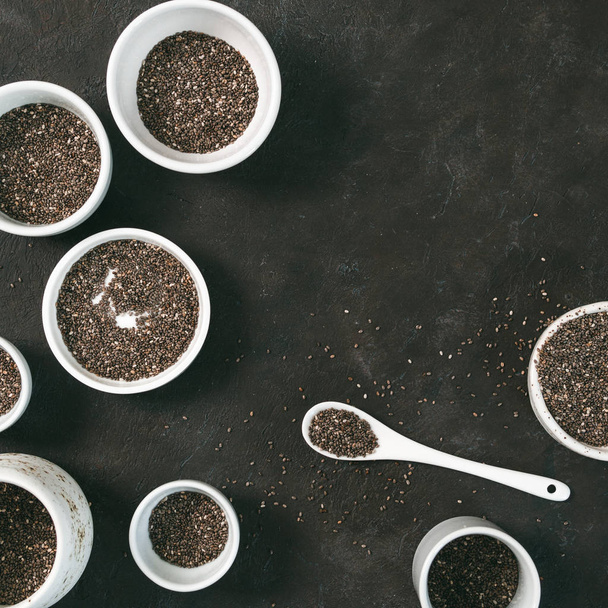 Organic chia seeds on black tabletop. Set of small bowls with organic chia seed. Superfood concept. Copy space. Top view or flat-lay. - Foto, Imagem