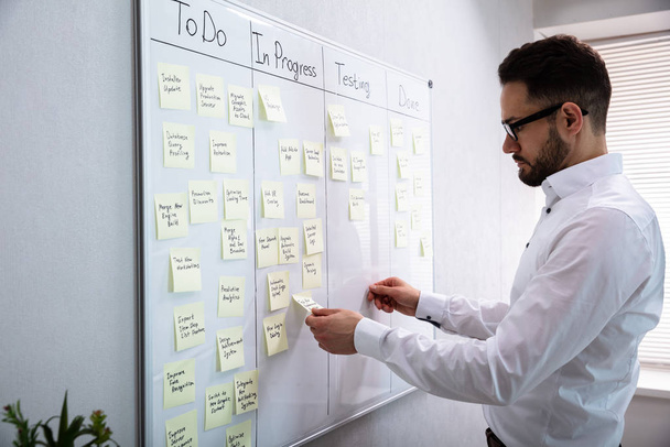 Side View Of Businessman Writing On Sticky Notes Attached To White Board In Office - Foto, Bild