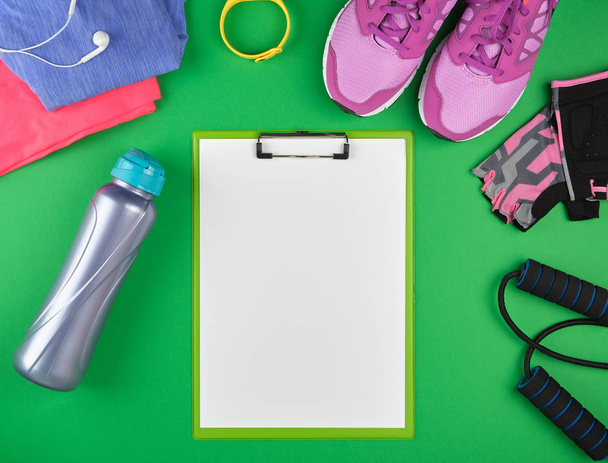 sports women's clothing for sports and fitness, top view, green background, in the middle of the holder for the paper with empty white sheets - Foto, Imagem