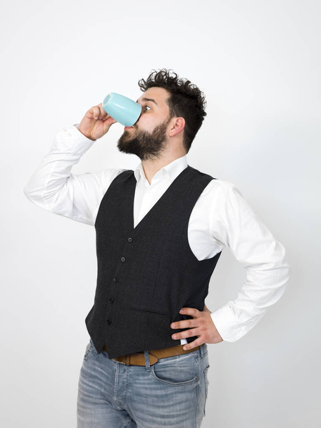 handsome, young man with black beard posing with turquoise coffee cup or tea cup in front of white background and making different facial expressions - Photo, Image