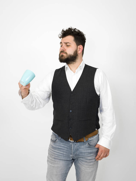 handsome, young man with black beard posing with turquoise coffee cup or tea cup in front of white background and making different facial expressions - Photo, image