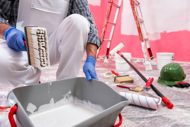 Caucasian house painter worker in white overalls, prepare the white paint to paint the pink wall. Construction industry. Work safety. - 写真・画像