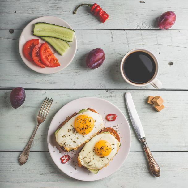 Breakfast toasts with vegetables and fried egg on white plate, cup of coffee and some fruits over wooden background. Healthy food concept. View from above. - Foto, Imagem