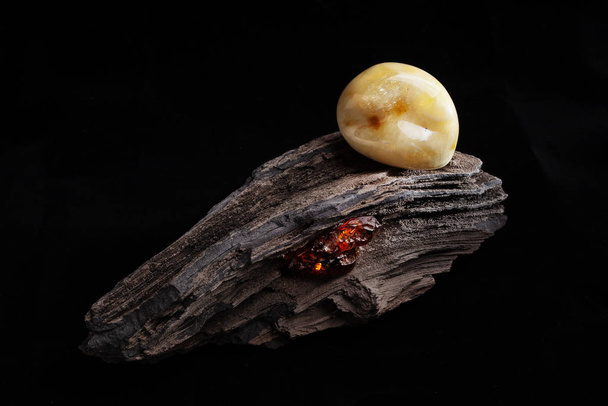 A piece of yellow semi opaque natural amber, classification color Bastard, has cracks inside. Polished, has a bead shape. Placed on dark stoned wood texture. - Фото, зображення