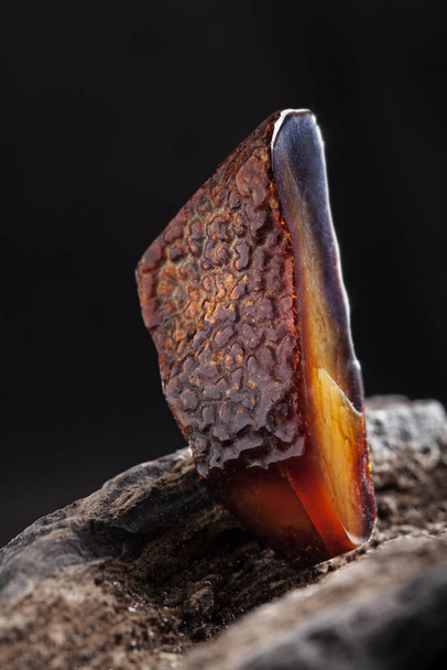 A piece of dark red semi transparent natural amber, classification color cherry or dragon blood, has cracks on its surface. Polished, oval shape. Placed on dark stoned wood texture. - Fotó, kép
