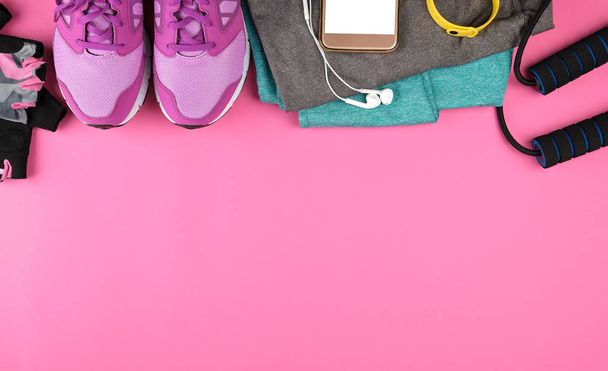 women's sportswear for sports and fitness, next to a smartphone with a blank white screen and headphones, pink background, top view, copy space - Photo, Image