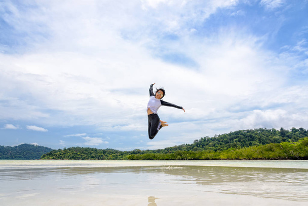 Felice giovane donna asiatica con gli occhiali da sole che salta divertimento sulla spiaggia di Ko Ra Wi-Fi sul cielo blu in riva al mare in vacanza vacanza vacanza estiva a Lipe Island nel Parco Nazionale di Tarutao, Satun, Thailandia
 - Foto, immagini