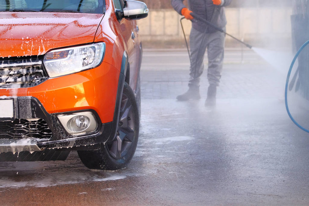 El hombre lava su coche naranja en el lavado de autos. Limpieza con un chorro de agua en el auto-servicio de lavado de coches.
. - Foto, Imagen