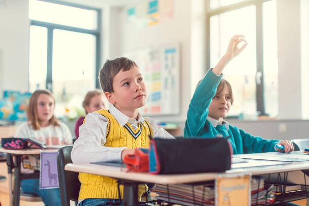 Хлопчик студент в класі знає відповідь піднявши руку
 - Фото, зображення