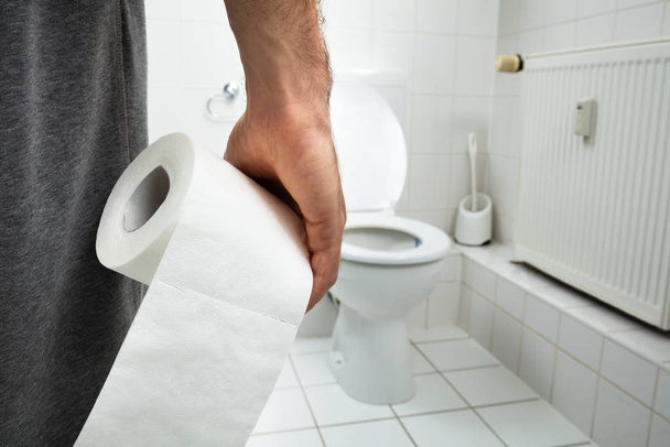 Man Suffers From Diarrhea Holding Tissue Paper Roll Standing In Front Of Toilet Bowl - Valokuva, kuva
