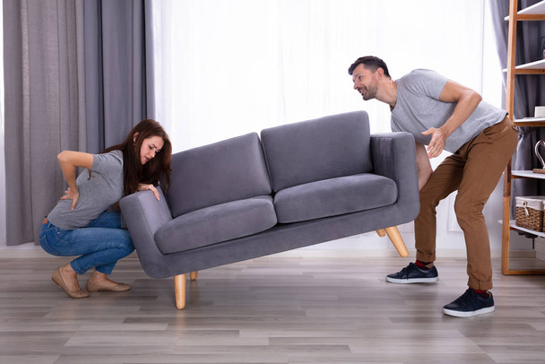 Young Man Looking At His Wife Suffering From Back Pain While Lifting Sofa - Photo, Image