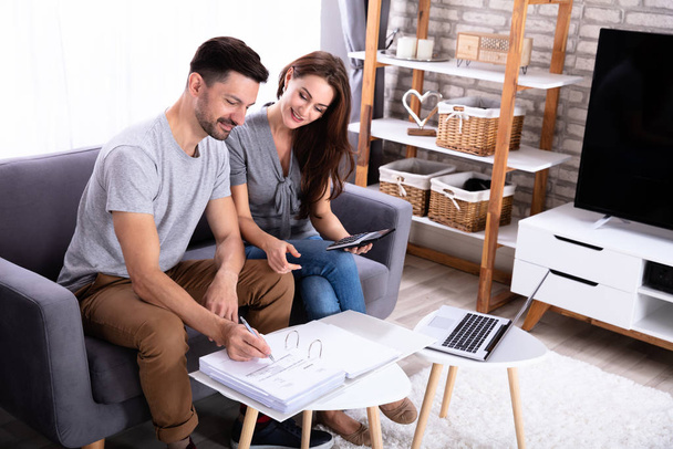 Smiling Young Couple Sitting On Sofa Calculating Invoice At Home - Foto, Bild