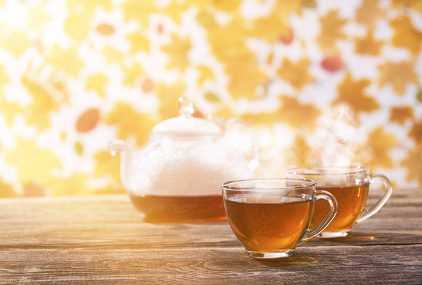 φλιτζάνι τσάι με τσαγιέρα μια ηλιόλουστη μέρα του φθινοπώρου σε ξύλινο φόντο - Φωτογραφία, εικόνα
