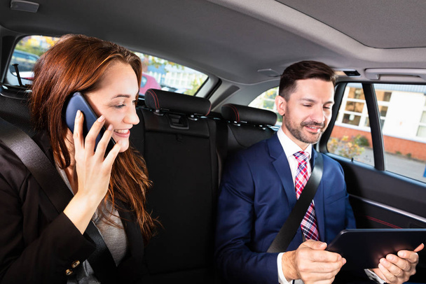 Happy Young Businesswoman Sitting Inside Car Beside Her Male Colleague Using Smartphone - Foto, immagini