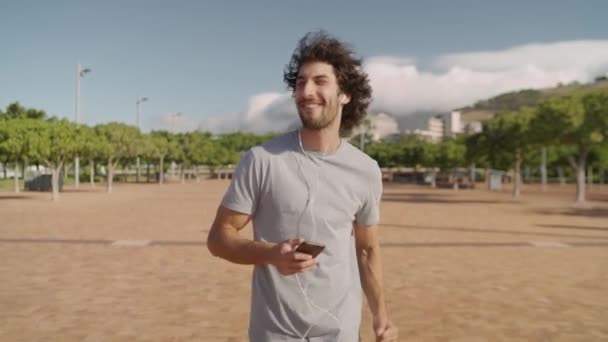 Cheerful and carefree caucasian young man dancing while listening to music on earphones in the park - a happy man in the park - Imágenes, Vídeo
