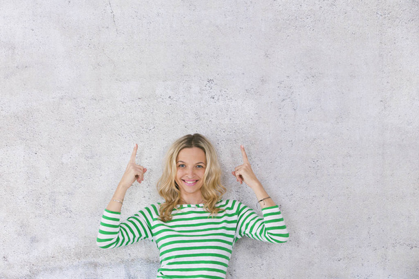 beautiful, young, pretty blonde business woman posing in front of a concrete wall and wearing green, white striped sweaters - Fotó, kép
