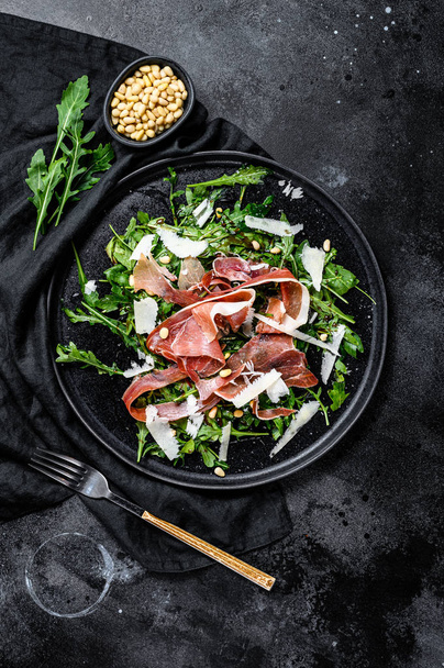 Salad with Serrano jamon, ham, rucola and Parmesan cheese. Black background, top view. - 写真・画像