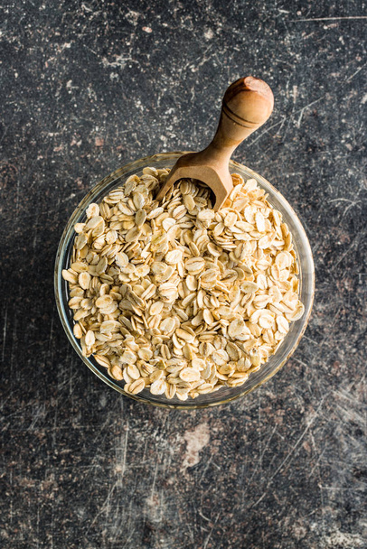 Dry rolled oatmeal in bowl and wooden scoop. - Foto, afbeelding