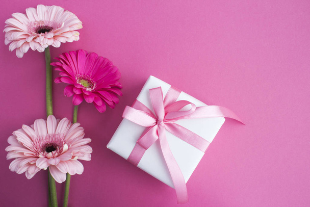 Gift with pink bow and pink flowers on the pink background.Top view.Copy space. - Foto, Bild