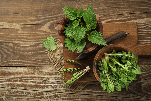 Spring healthy food. Nettle and dandelion leaves on wooden background - Фото, изображение