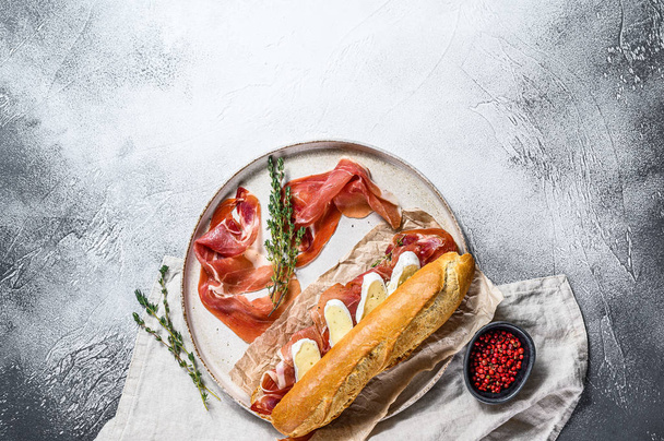 Baguette szendvics sonkával, Camembert sajttal tálcán. Szürke háttér, felülnézet, hely a szövegnek - Fotó, kép