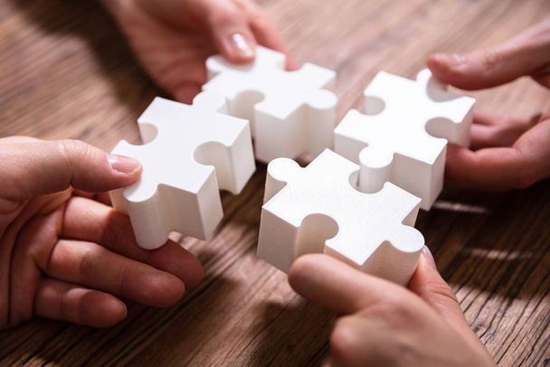 Close-up Of Businesspeople Solving White Jigsaw Puzzle Together On Wooden Desk - Fotografie, Obrázek