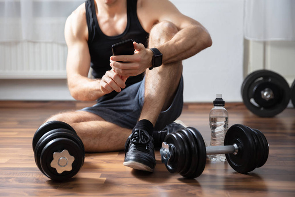 Man Sitting On Hardwood Floor In Gym Using Smartphone - Photo, Image