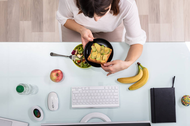 An Overhead View Of Businessperson's Hand Eating Salad With Fork On Desk - Фото, изображение