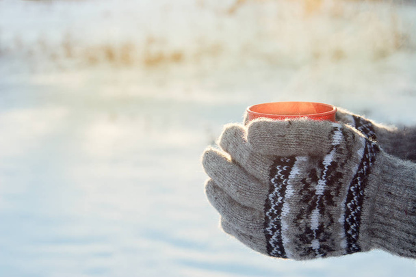 mug with hot drink in hands dressed in knitted wool mittens in winter on a Sunny frosty day, winter picnic, winter mood - Photo, Image