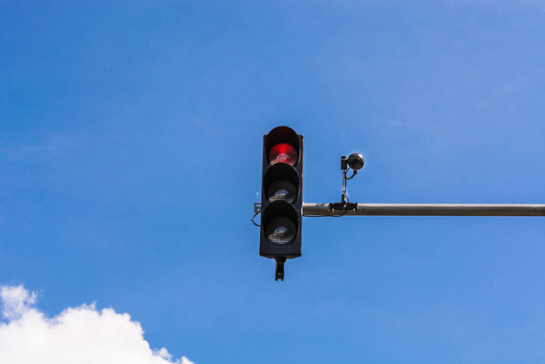 A traffic light and a surveillance camera on a pole mounted on the street. - 写真・画像
