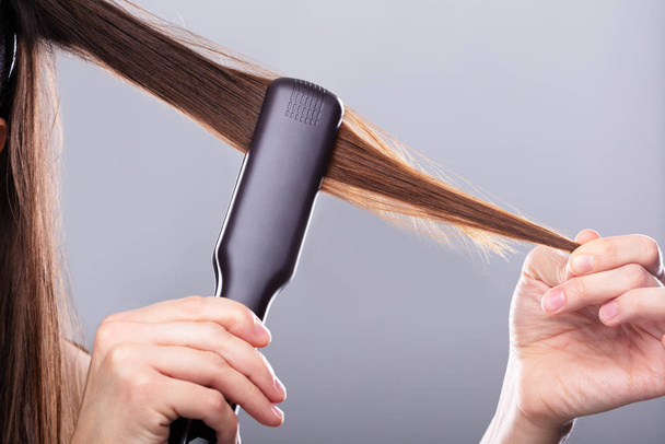 Close-up Of Woman Straightening Hair With Straightener Against Gray Background - Foto, Imagen
