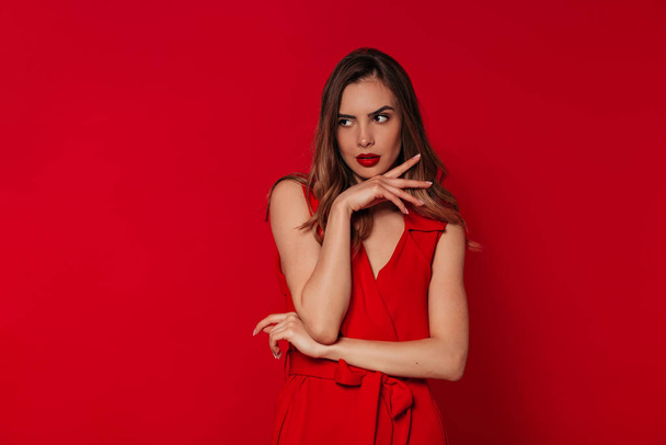 Blissful woman with evening make up wearing red dress posing over red background in studio. Portrait of european confident woman  - Photo, Image